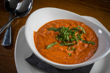 Creamy Tomato Soup garnished with Basil on a wooden board