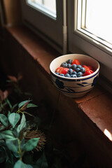Plate with fresh berries on the windowsill. Strawberries and blueberries