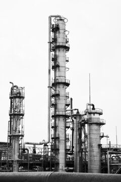 Old methanol distillation rectification refinery column towers and reactors under grey sky at chemical plant enterprise. Industrial black and white BW background vertical with copy space.