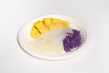 Mango sticky rice on a white paper plate on a white background, topped with coconut milk.