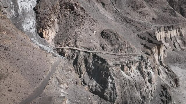 Aerial View Of Winding Old Silk Road Through Rugged Arid Mountains Beside River. Circle Dolly With Dolly Back Reveal Of Valley Floor And River