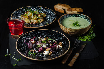Large lunch set of three courses soup, second course and salad. Business lunch set made of three meals. Salad with beetroot, olives, feta and nuts. Cream soup and frying pan with sausages and compote.
