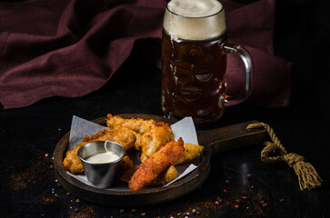 Spicy fried breaded chicken wings on a wooden board and a glass of beer.