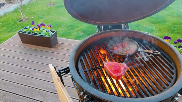 4K footage of a fresh raw tuna steaks cooked on an open fire on a kamado type barbeque grill and fresh vegetables on a cast iron 