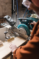 partial view of blurred woodworker cutting board with miter saw.