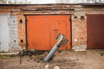 Close-up view stock image of real unexploded military missile, torpedo or shell stuck in ground near doors of garages outdoors. Moments of dreadful war of Russia against Ukraine in 2022