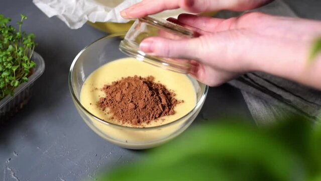 Making liquid chocolate dough for cake, pancakes or pie. Adding cocoa powder into batter and stirring it with a whisk in the glass bowl. Preparing a dessert