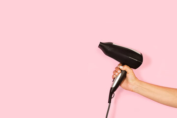 Fototapeta Mano de mujer sosteniendo un secador negro de pelo sobre un fondo rosa liso y aislado. Vista de frente y de cera. Copy space obraz