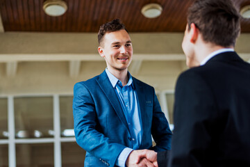 Two young men shaking hands close to a business building.Businessman and his partner agree deal outdoor.Businessman in formalwear negotiate corporate deal standing outdoor background. - obrazy, fototapety, plakaty