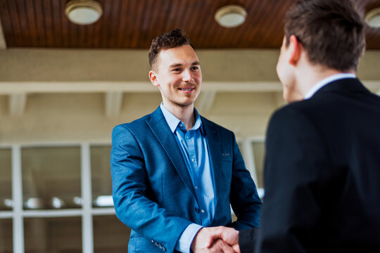Two young men shaking hands close to a business building.Businessman and his partner agree deal outdoor.Businessman in formalwear negotiate corporate deal standing outdoor background.