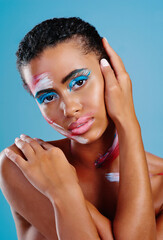 Colour me beautiful. Studio portrait of a beautiful young woman covered in face paint posing against a blue background.
