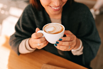 Top view photo of smiling adorable lady with wonderful smile, dark manicure is holding coffee and enjoying resting in cafeteria