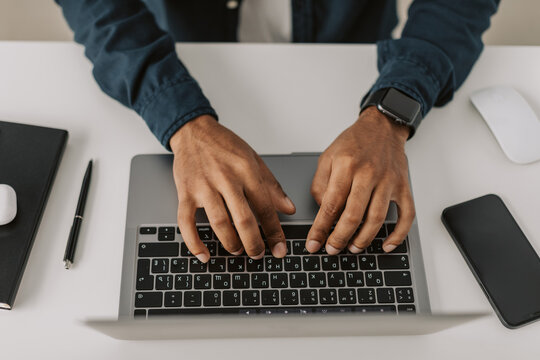 High angle view of one African american man typing and texting on laptop keyboard sitting in white airy office, indoor black adult student study online, crypto enthusiast searching stock