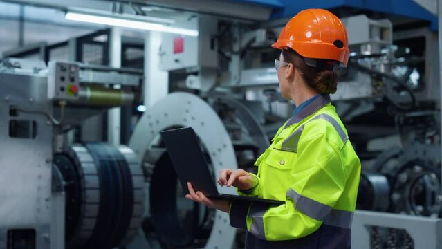Uniformed specialist working laptop computer on modern huge digital factory.