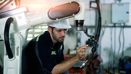 Engineer setting up automatic robotics welding arms in factory.