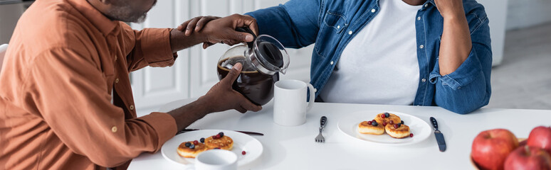 cropped view of senior african american man pouring coffee to wife during breakfast, banner.