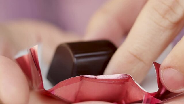 chocolate with liqueur and cherry. close up slow motion a woman's or girl hand is taking a little chocolate from a paper foil, candies from pink color wrapper.sugar addicted, unhealthy food concept.