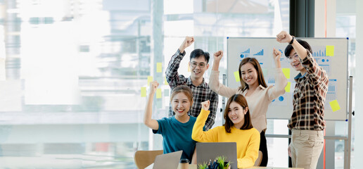 A group of startup company employees are in the conference room, raising their hands to show their appreciation after looking at the company's sales and profitable results. Startup company concept.