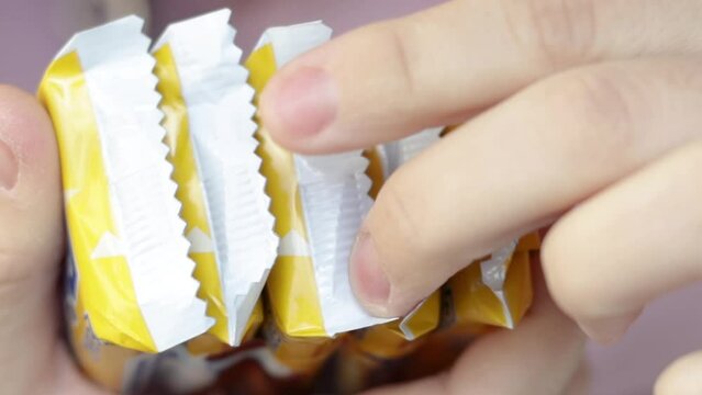 woman's hand is cutting some chocolate bars or cookies wrapped in plastic pack. sweets from shop, market, chocolate store. close up slow motion video. unhealthy food,sugar. yellow color packs.