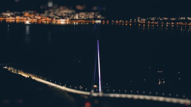 The H&aring;logaland Bridge near Narvik, Norway. The brightly lit suspension bridge spans above the dark water of the fjord. Night city with busy traffic in the background.