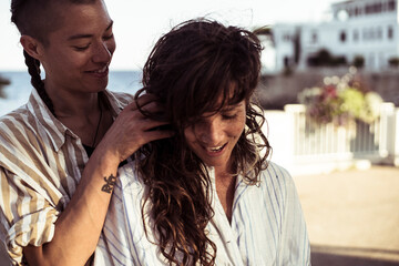 happy queer female couple smile affectionately by Mediterranean sea