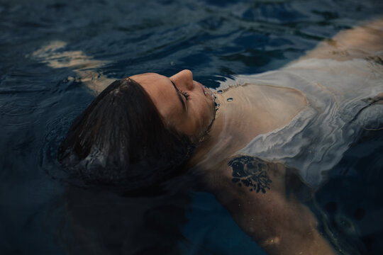 Adventurous young lady floating on back in backyard pool