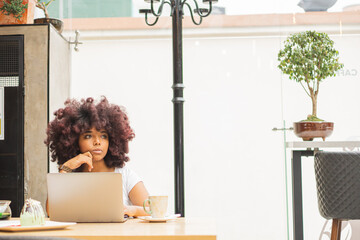 Young Afro woman in a coffee shop working online at her computer.