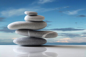 five grey stones balanced over white surface over blue sky
