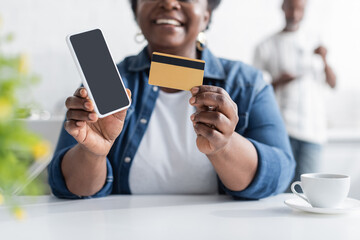 cropped view of happy senior african american woman holding credit card and smartphone with blank screen.