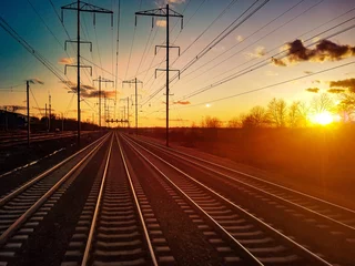 Papier Peint photo Chemin de fer Les voies ferrées se dirigent vers l& 39 horizon lointain avec une lumière colorée du coucher du soleil qui brille dans le paysage d& 39 arrière-plan