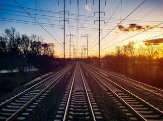 Fototapeta na wymiar Train tracks converging on the horizon landscape with colorful sunset light in the background sky