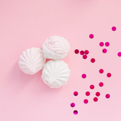 Three white gentle marshmallows on a pink background with festive confetti. Creative design of sweets