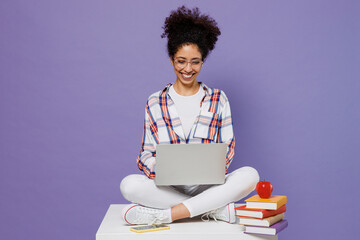 Full body smart young girl woman of African American ethnicity teen student in shirt hold use work on laptop pc computer isolated on plain purple background. Education in university college concept.