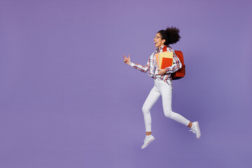 Full size excited happy young girl woman of African American ethnicity teen student in shirt hold backpack jump high hurry up run fast isolated on plain purple background Education in college concept