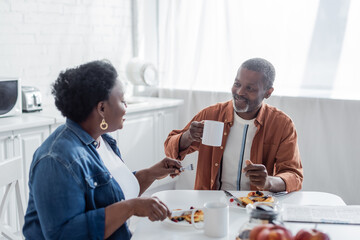 smiling african american man talking with senior wife during breakfast.