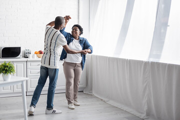 full length of cheerful senior african american couple dancing in kitchen. - Powered by Adobe