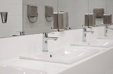 Modern public toilet interior. Many sinks with faucets for washing hands.