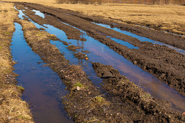 Rural dirt or unpaved road with mud and slush in countryside field in sunny summer or spring weather