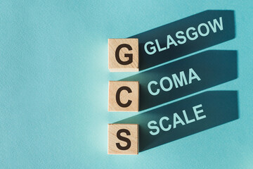 GCS Glasgow Coma Scale text, written on wooden blocks with shadows on blue background.