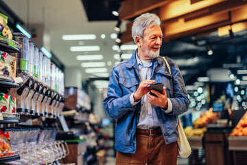 Smiling senior man using phone in grocery store