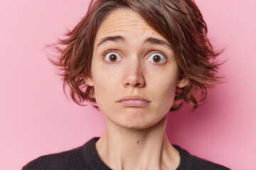 Close up shot of embarrassed woman with hairstyle has widely opened eyes from fright feels worried...