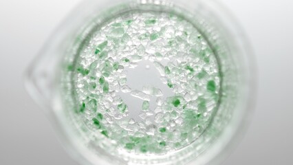 Top view shot of beaker with crystals of green salt in water on light grey background | Mineral skin care cosmetics formulation concept