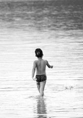 boy walking in the shallow water of a lake with sky reflection