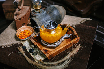 A teapot with sea buckthorn tea standing on the table. A plate with sea buckthorn berries. Antique iron. An old newspaper