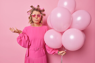 Obraz na płótnie Canvas Crying displeased woman with leaked makeup wears shades and dress stands upset has spoiled party makes hairstyle holds bunch of inflated balloons isolated over pink background. Monochrome shot