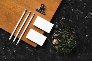 Branding identity mockup. Blank business cards, pencils, succulent plant, metal clip and wooden board on black plaster background. Flat lay. - obrazy, fototapety, plakaty
