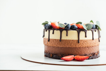 Brown layered cake Three chocolates decorated with blueberries, strawberries and chocolate drips on top. White background. Close-up