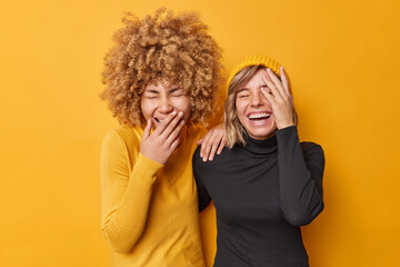 Photo of overjoyed friendly women laugh out loudly giggle as hear funny joke have fun chuckle at camera feel positive dressed in casual turtlenecks isolated over yellow background. Happiness concept - obrazy, fototapety, plakaty