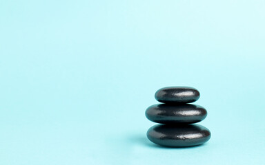 A stack of black zen balance stones on a blue background. The concept of a SPA center. A stage for promotion, sale, presentation or cosmetics. Copy space