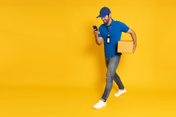 Delivery man holding parcel box and mobile phone and walking isolated on yellow background, Online...